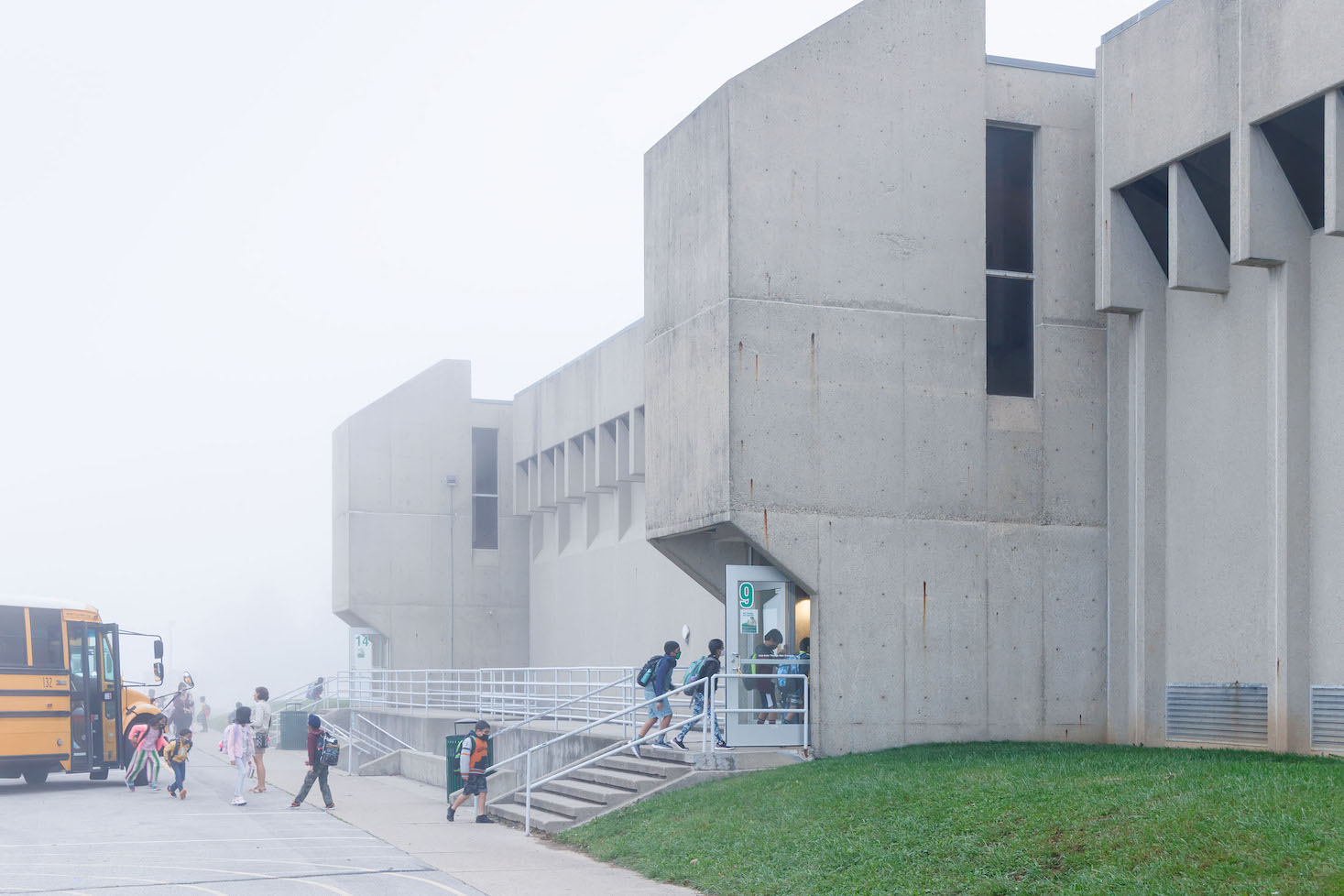 Children walking off their school bus into the Brutalist concrete Southside Elementary School building.