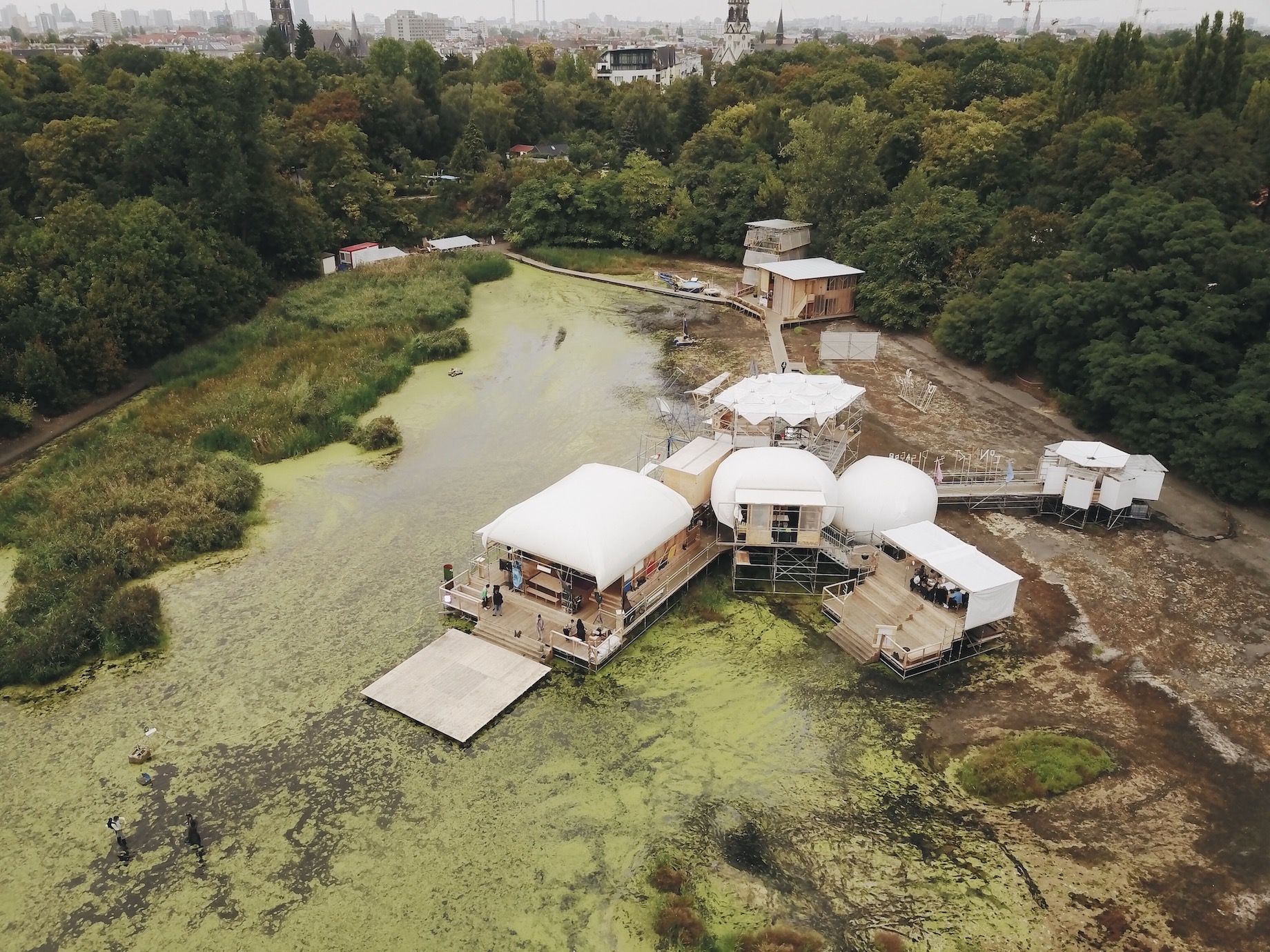 Berlin’s Floating University, in the middle of a body of water with greenery around it and a city beyond.