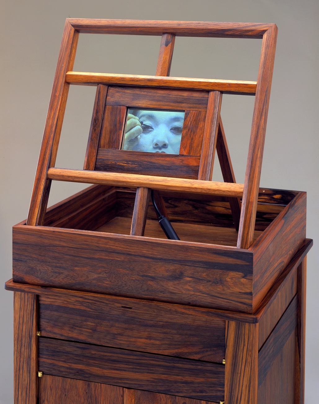 Square wooden vanity with built-in picture frame at the top holding an image of a woman applying eyeliner