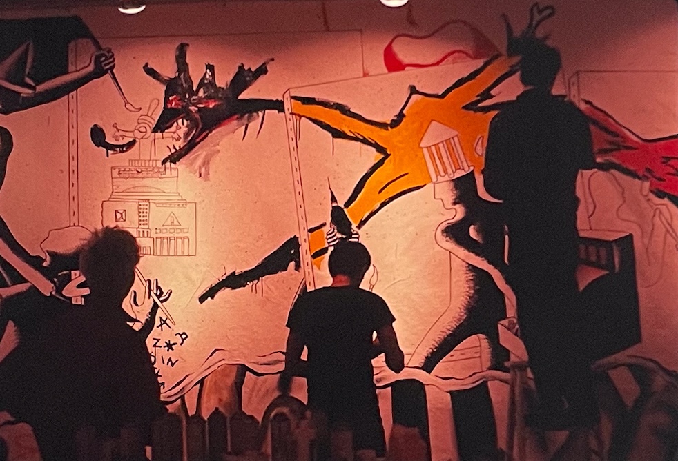 Three people paining an abstract fantastical mural on a wall of the JNP&P gallery space, in 1986