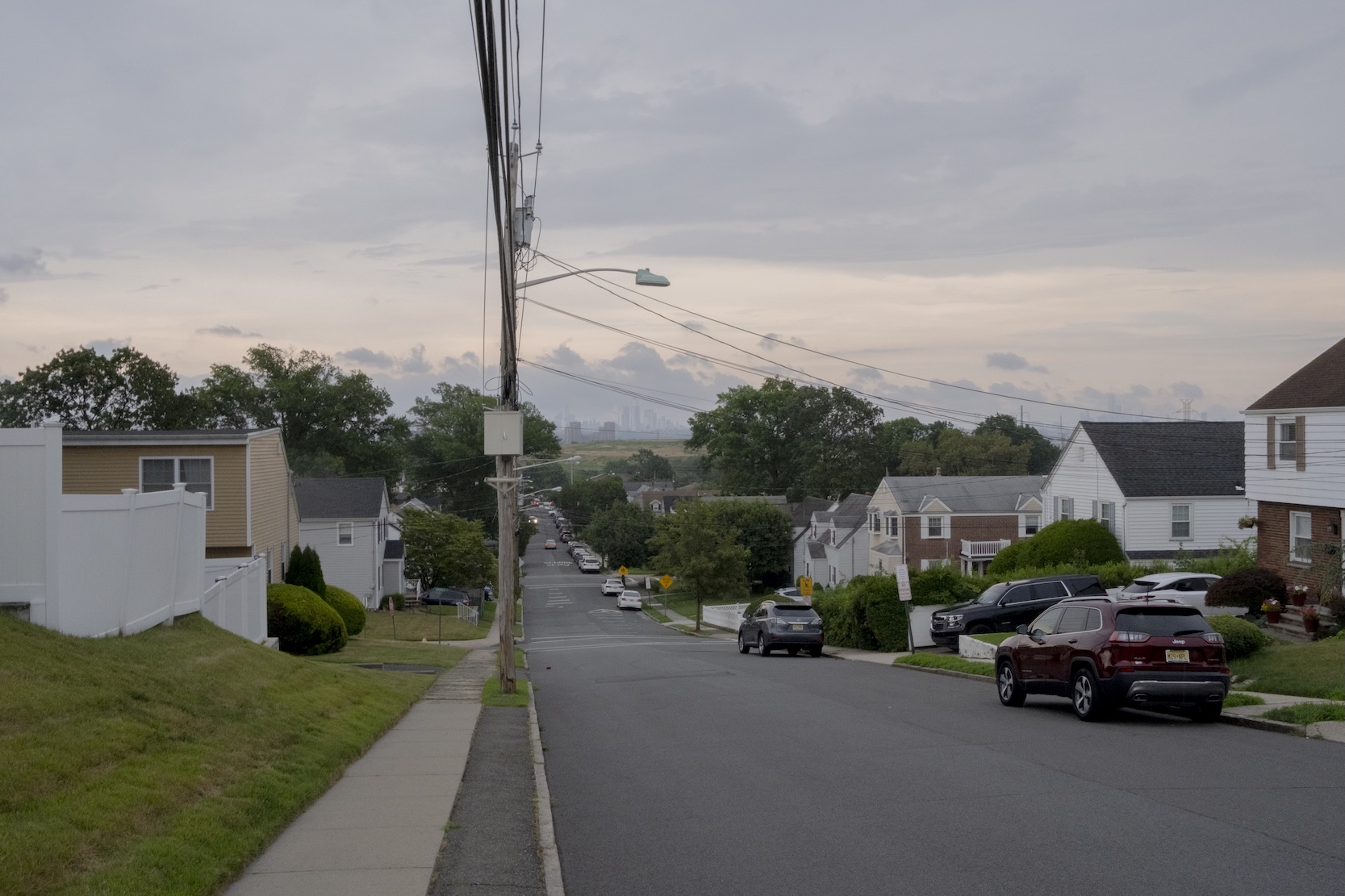 Suburban New Jersey street at dusk with New York City skyline in background